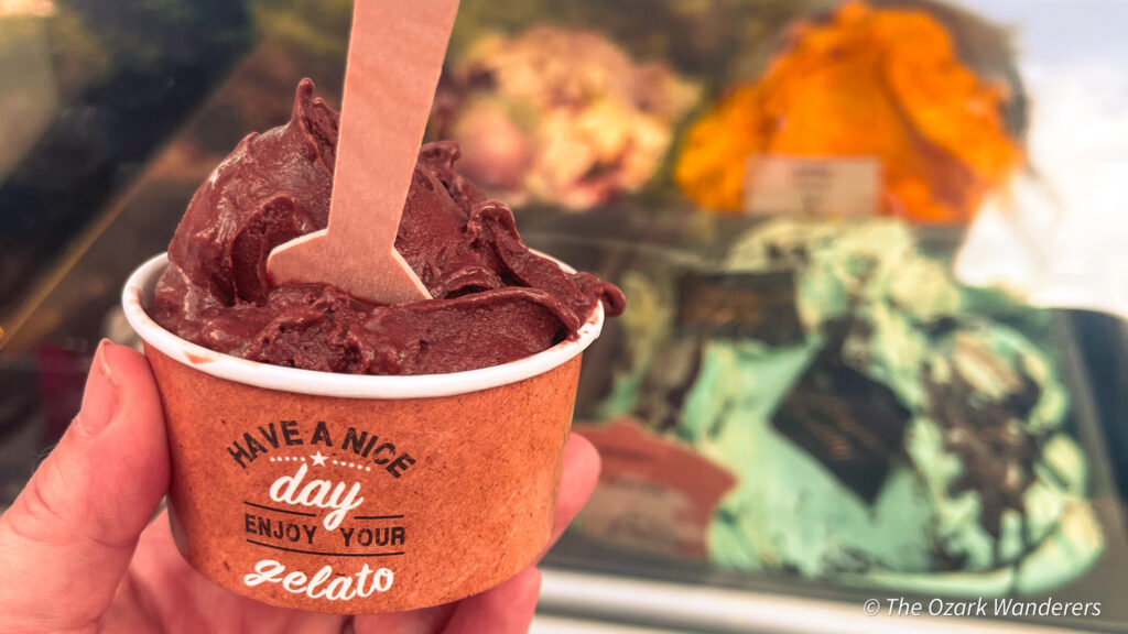 Cup of rich chocolate gelato held in front of a colorful gelato counter in Palma de Mallorca, Spain.