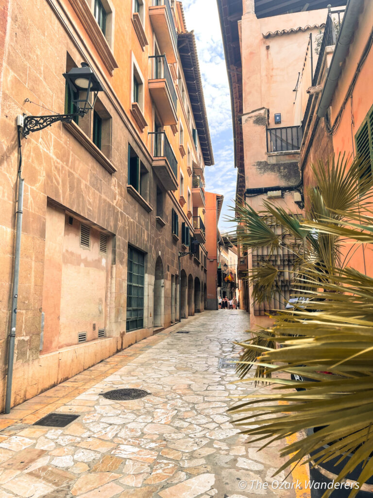 Narrow cobblestone street lined with warm stone buildings in the Old Town of Palma de Mallorca, Spain.